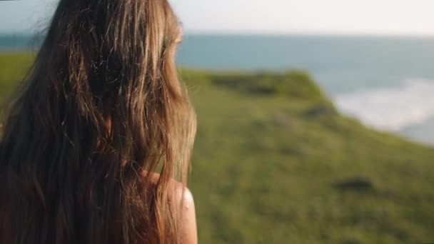 Close-up Asia strand bokeh: vrouw kijken op watergolf in de zomer zon dag. Meisje op hoog groen gras klif — Stockvideo