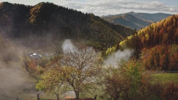 Aérea de nubes de neblina sobre el pueblo de montaña de otoño. Campos, bosque en cabañas en niebla ahumada — Vídeos de Stock