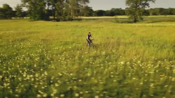 Дівчата їздять на велосипеді на сонячному лузі. Жінка їде на велосипеді на квітках. Сільський ландшафт природи — стокове відео
