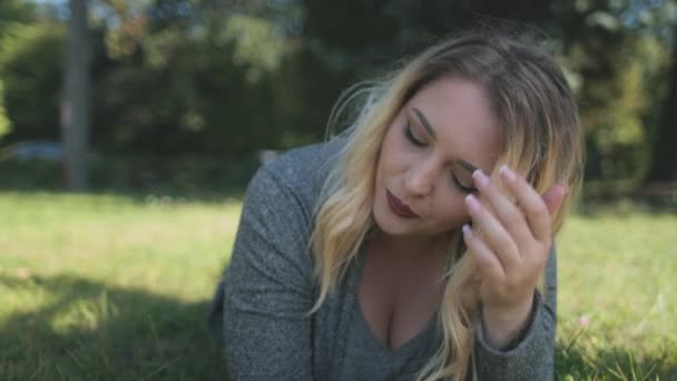 Mulher loira falando close-up telefone. Menina atraente plus size lay, sorriso na grama. Natureza paisagem — Vídeo de Stock