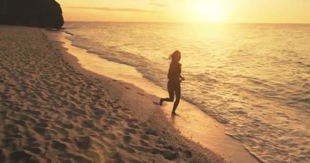 Femme bronzée courant à l'antenne du coucher du soleil doré. Paysage marin nature d'été avec plage de sable au coucher du soleil — Video
