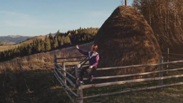 Woman with mobile at mountain aerial. Autumn nature landscape. Girl tourist on wood fence. Haystack — Stock Video
