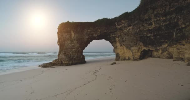 Sol buraco arco natural na parede do penhasco na costa oceânica closeup aéreo. Atração turística na praia de areia — Vídeo de Stock