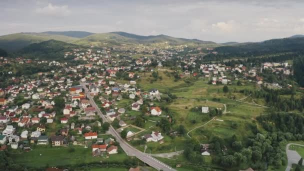 Mountain town on green grass hill aerial. Road with car at cottages. Nature landscape. Spring forest — Stock Video