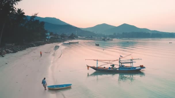 Playa del océano de la mañana con barcos de pesca en la luz rosa amanecer. Mar tropical tranquilo, gente comenzando un nuevo día. — Vídeo de stock