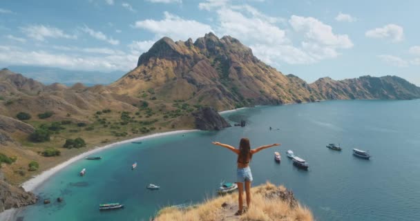 Woman raise hands on mountain top. Aerial summer tropical landscape. Blue sea water bay with boats — Stock Video