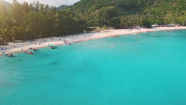 Vue aérienne île d'eau bleue claire avec palmiers et montagnes rétro-éclairés. Les touristes marchent au bord de la mer. — Video