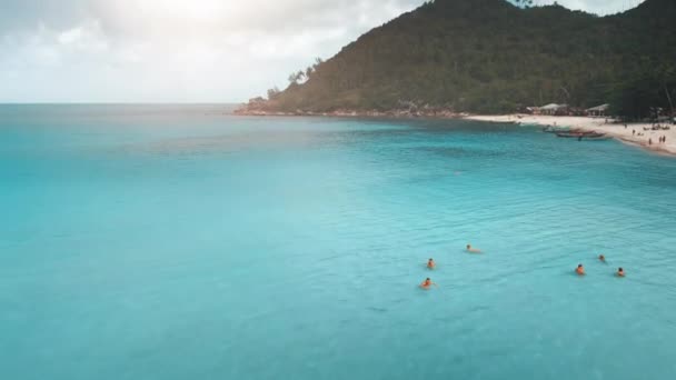 Εναέρια μπλε ηλιόλουστη καθαρή θάλασσα κοντά στην παραλία. Πράσινο βουνά τροπικό νησί. Οι άνθρωποι κολυμπούν στον γαλάζιο ωκεανό. — Αρχείο Βίντεο