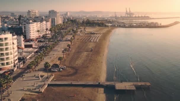 Pôr do sol aéreo sobre a praia da cidade com palmeiras. Casas perto do mar. Luz solar em navios no porto no cais. — Vídeo de Stock