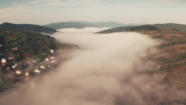 Niebla gris gruesa aérea sobre las cumbres montañas y árboles verdes, casas de pueblo en valle. Bosque denso. — Vídeo de stock