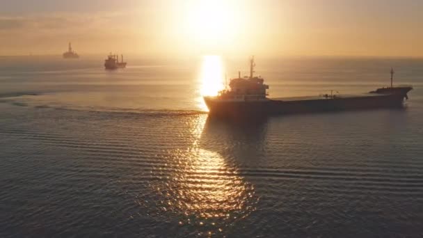 Luftaufnahme, orangefarbener Sonnenaufgang über Schiffen im Ozean. Wellen im blauen Wasser. Gütertransport auf dem Seeweg. — Stockvideo