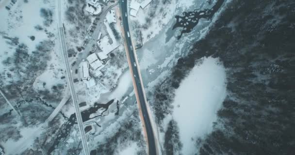 Luftstraße über Brücke über zugefrorenen Fluss und verschneite Landschaft. Dünnes Eis auf kaltem dunklen Wasser. — Stockvideo