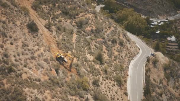 Aerial view, construction an asphalt road on mountain ridge. Excavator digs ground on hill. Nature — Stock Video