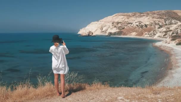 Blogueur de voyage faisant la photo du lagon bleu de la mer debout sur le sommet de la colline. Vue de derrière. Contexte d'été. — Video