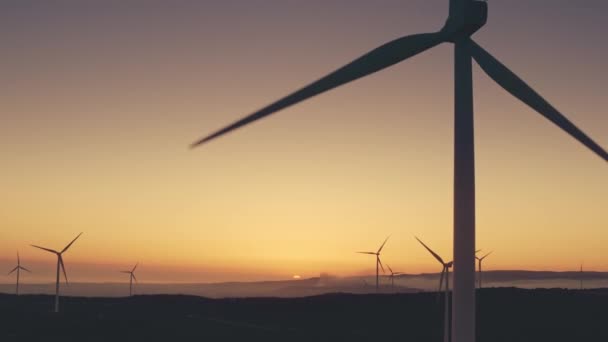 As turbinas de pás de vento produzem energia alternativa à luz do pôr-do-sol. Moinhos de vento modernos giram — Vídeo de Stock