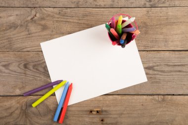 Boya kalemleri ve ahşap masada boş bir sayfa.