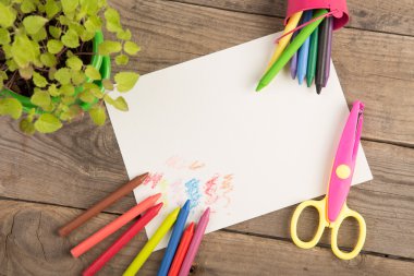 Boya kalemleri ve ahşap masada boş bir sayfa.