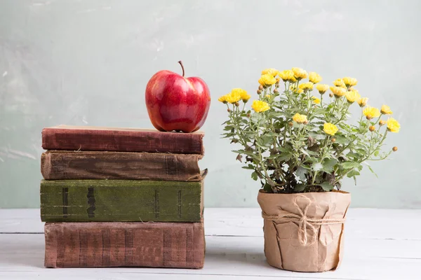 Maçã em uma pilha de livros na mesa com flores — Fotografia de Stock