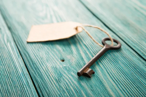 Oude roestige sleutel met een papieren etiket op de houten plank — Stockfoto