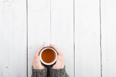 Süveter giymiş bir kadının elleri ahşap masada çay tutuyor.