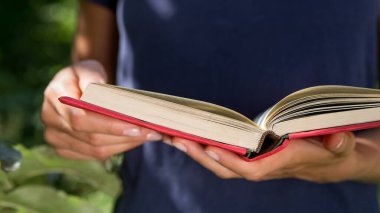 Yaz konseptinde okuma ve eğitim, açık bir kitap tutan kız, açık havada bahçede kitap okuyan kız.