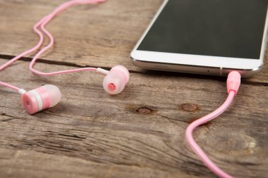 Eski ahşap tahtada pembe kulaklıklı beyaz akıllı telefon.