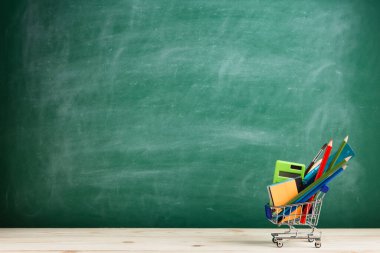 Eğitim konsepti - oditoryumun masasındaki alışveriş arabasında okul malzemeleri