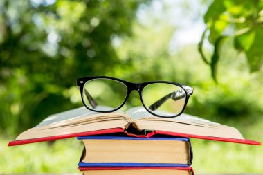 Bahçedeki ahşap bir masada açık kitap ve gözlük. Güneşli bir yaz günü, bir tatil konseptinde okumak.