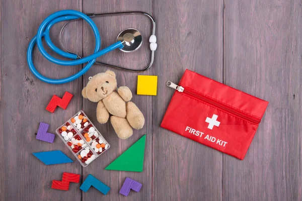 Little toy bear, stethoscope and first aid kit on the wooden desk - children health care concept, pediatrist workplace