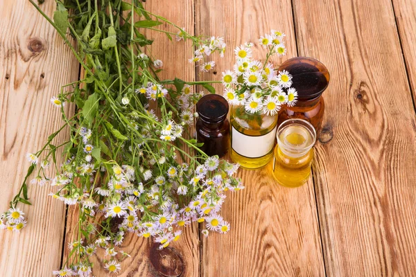 Herbal medicine concept - bottles with camomile and oil on woode — Stock Photo, Image