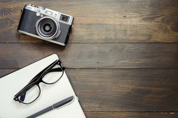 Kamera, Brille und Notizblock auf Holzgrund — Stockfoto