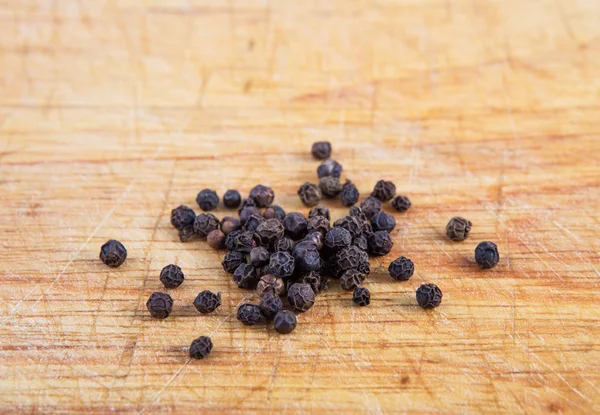 Zwarte peper zaden op een houten bord — Stockfoto