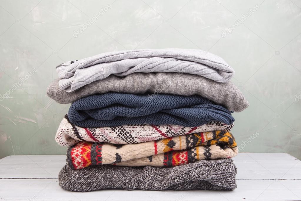 warm sweaters stacked on wooden table