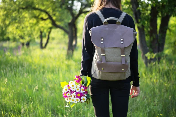 Młoda kobieta piesze wycieczki z plecaka i kwiatów w ręku — Zdjęcie stockowe