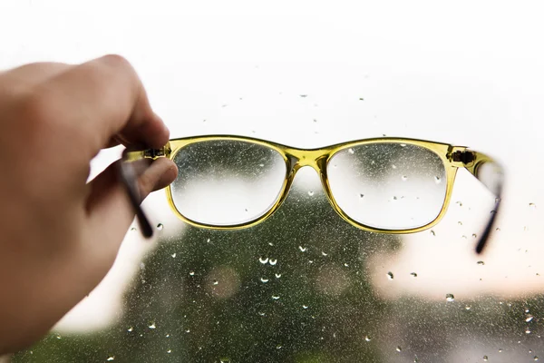 Γυαλιά ανάγνωσης στο χέρι σε φόντο παράθυρο βροχερή — Φωτογραφία Αρχείου