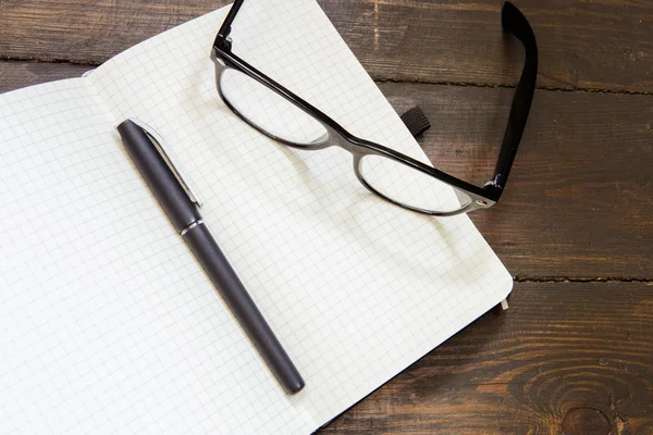 Lectura de gafas y bloc de notas sobre fondo de madera — Foto de Stock