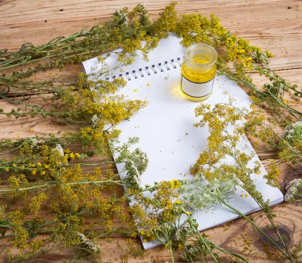 Olio da massaggio in bottiglia di vetro, erbe aromatiche e blocco note sul tavolo di legno — Foto Stock