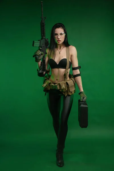 緑の背景にアメリカの自動小銃を持つ軍事疲労の細い女性 — ストック写真