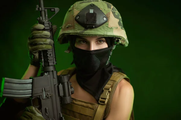 Woman in military uniform with an American automatic rifle in a helmet and Balaclava on a green background — Stock Photo, Image