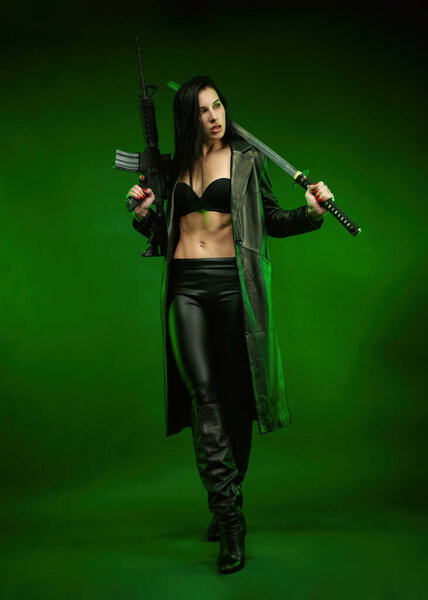 стройная женщина в черном кожаном плаще с американской автоматической винтовкой и катаной на зеленом фоне