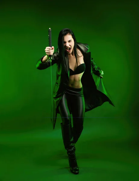 Mujer delgada en una capa de katana de cuero negro sobre un fondo verde —  Fotos de Stock