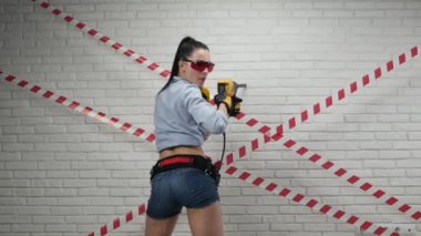 Kısa şortlu, elinde bir zımba tutan inşaat işçisi görüntüsünde seksi bir kadın.