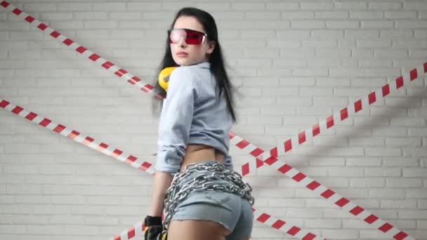 Una mujer en la imagen de un constructor en pantalones cortos bailando contra una pared de ladrillo — Vídeo de stock