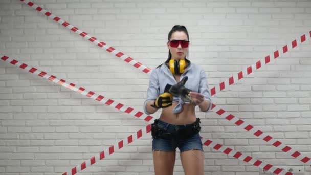 Sexig kvinna i bilden av en byggarbetare i korta shorts sätter på handskar — Stockvideo