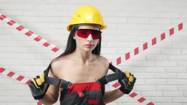 Portrait of a sexy woman in construction overalls and hard hat Baring her shoulders — Stock Video