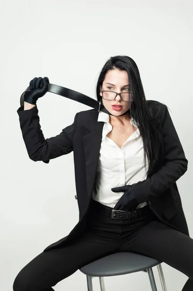 Une femme en vêtements et gants de bureau noirs est assise sur une chaise avec une ceinture autour du cou — Photo