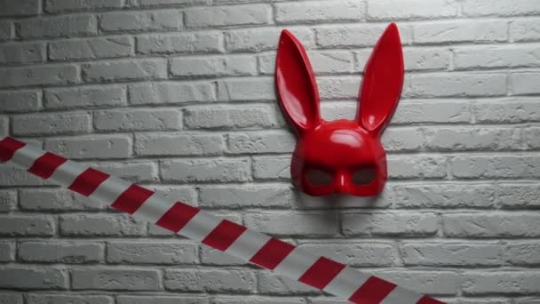 Röd kaninmask på en vit tegelvägg och röd och vit signaltejp — Stockvideo