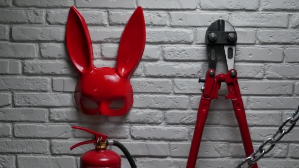 Diseño creativo de una pared de ladrillo de fuego con una máscara de conejo, extintores de incendios y cortador de pernos con una cadena estirada — Vídeos de Stock
