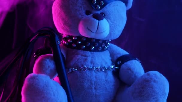 Urso de brinquedo vestido com cinto de couro arnês acessório para jogos BDSM em um fundo escuro em luz de néon na fumaça — Vídeo de Stock