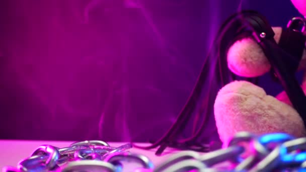 Ein Spielzeugbär trägt Ledergürtel, ein BDSM-Accessoire ist mit einem Schloss in Neonlicht angekettet — Stockvideo